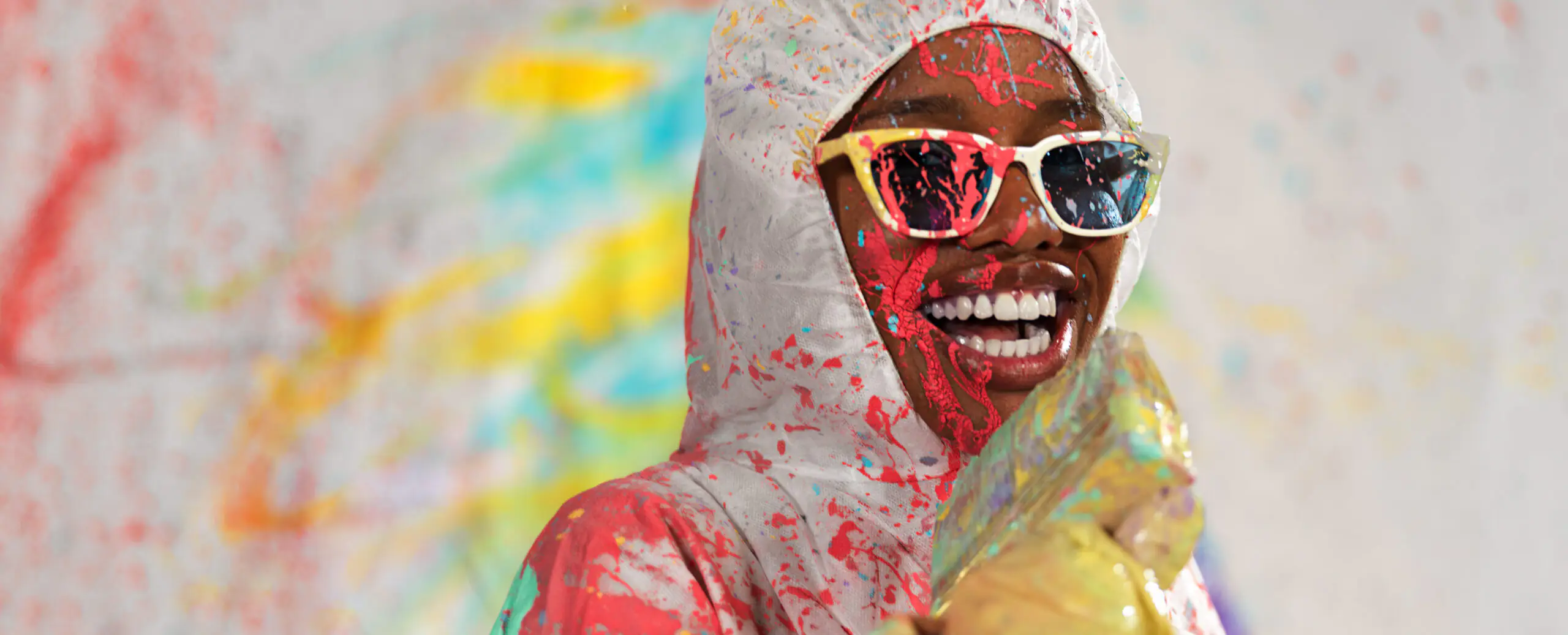 A IAAD. student wearing sunglasses and a white jacket smiles full of paint during the shooting of IAAD. community video